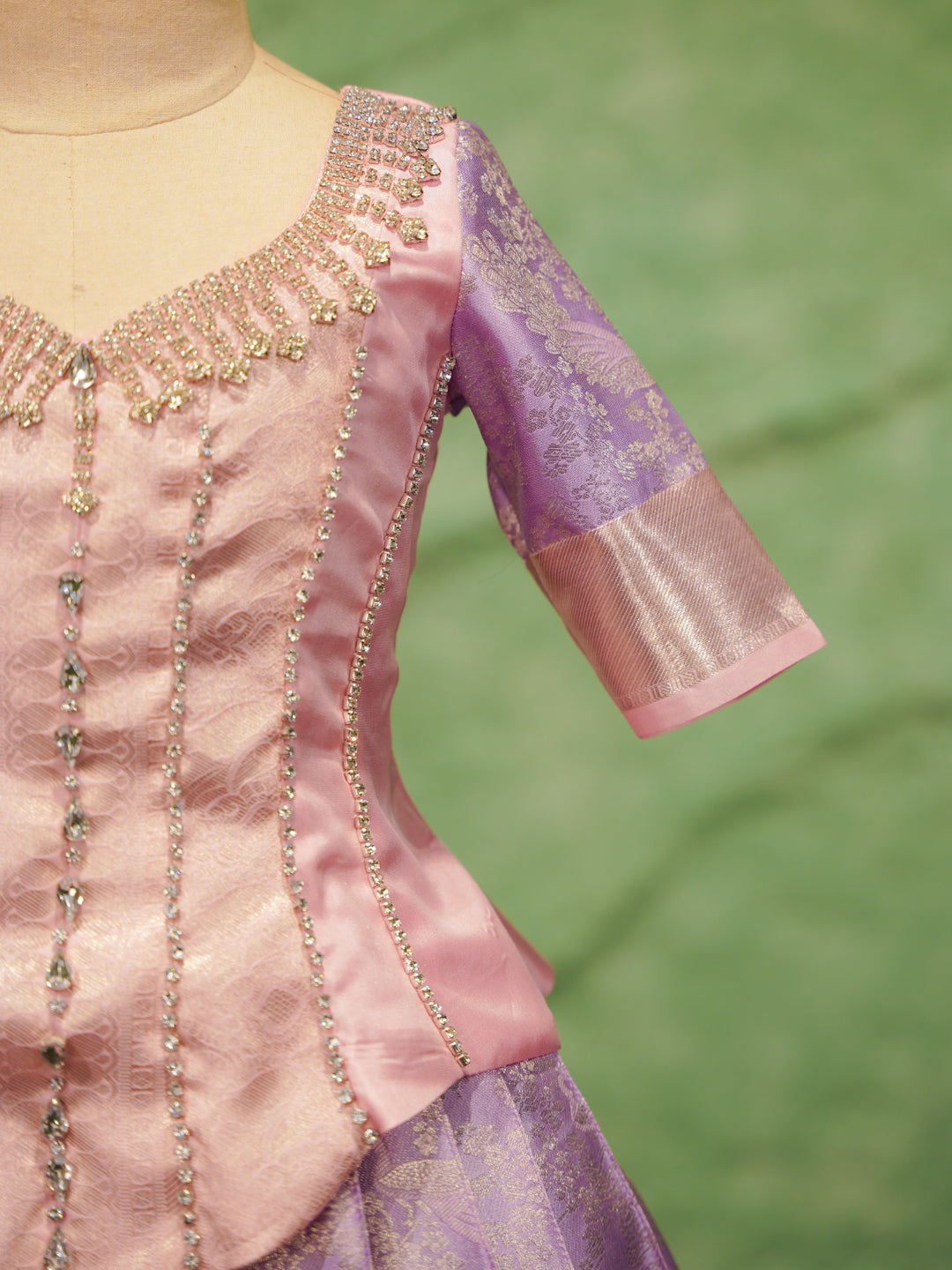 Close-up of a pink and purple traditional outfit with intricate detailing on a green background