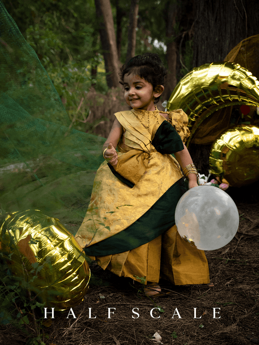 Grandeur Emerald Augustan Kanjivaram Silk Ball Gown for Baby Girl with floral jacquard pattern, puff sleeves, and a twisted gold-green bow on the waistline.